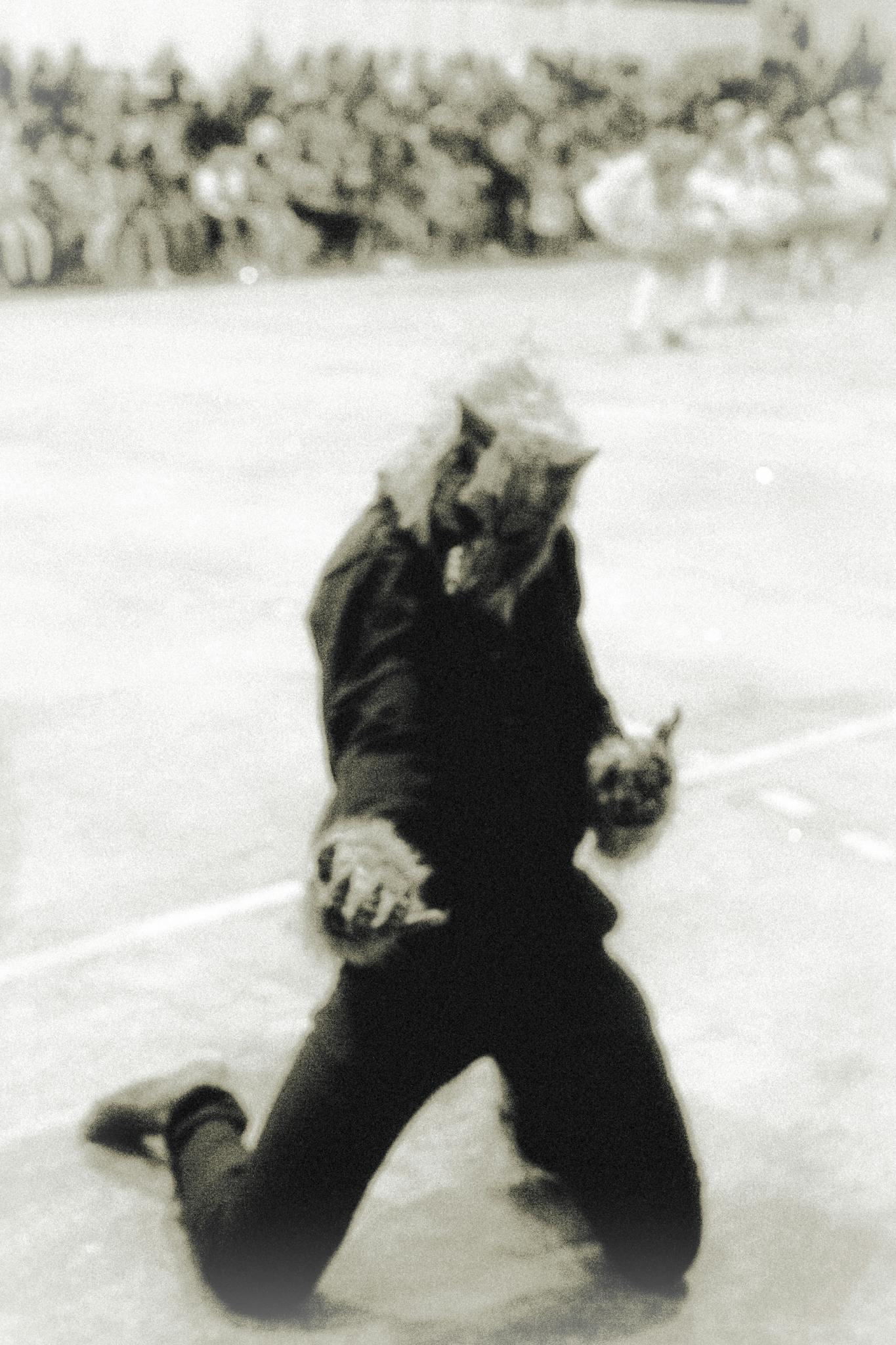 A costumed individual kneels outdoors, wearing a scary wolf mask in a dramatic pose.