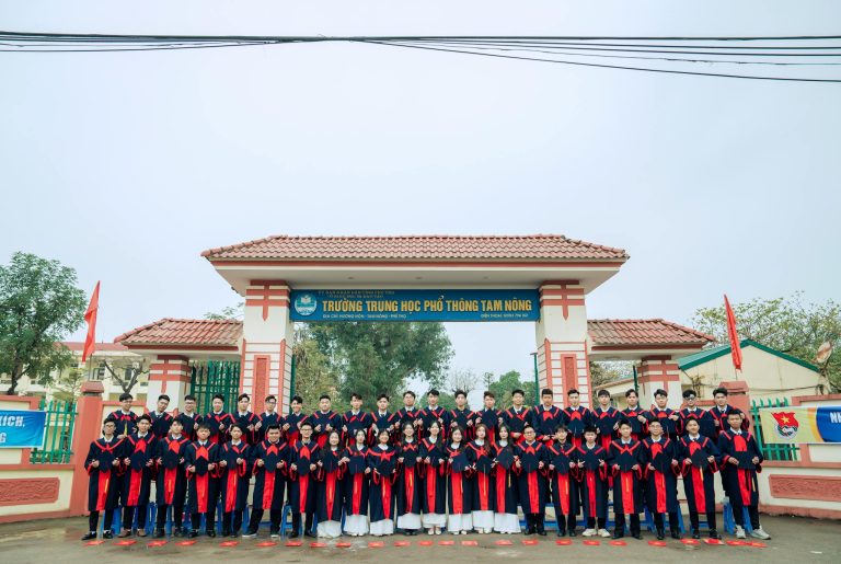 Group of students in graduation uniforms at Tam Nong High School entrance.