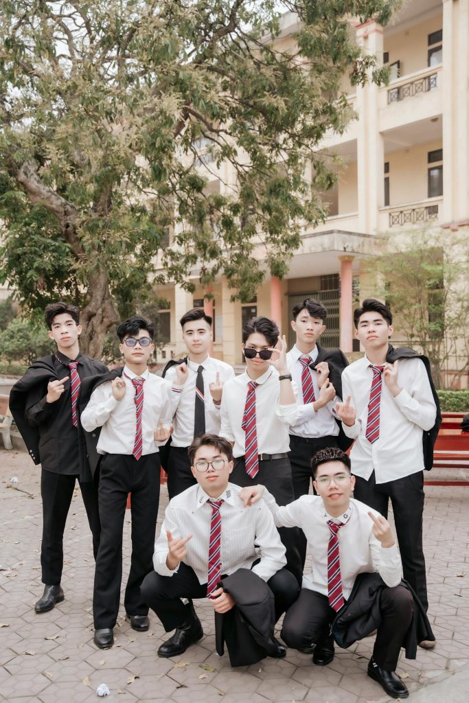 Group of teenagers in formal attire celebrating school graduation outdoors.