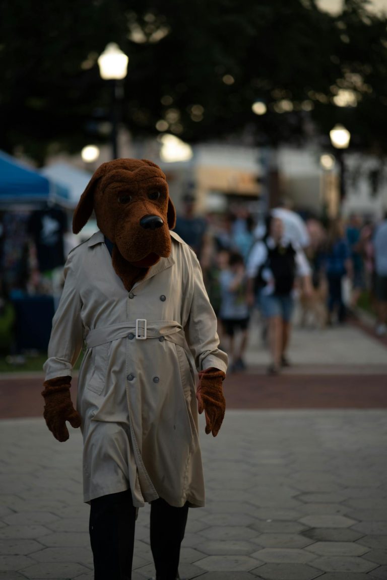 Person in dog costume wearing trench coat at a lively outdoor festival scene in the evening.
